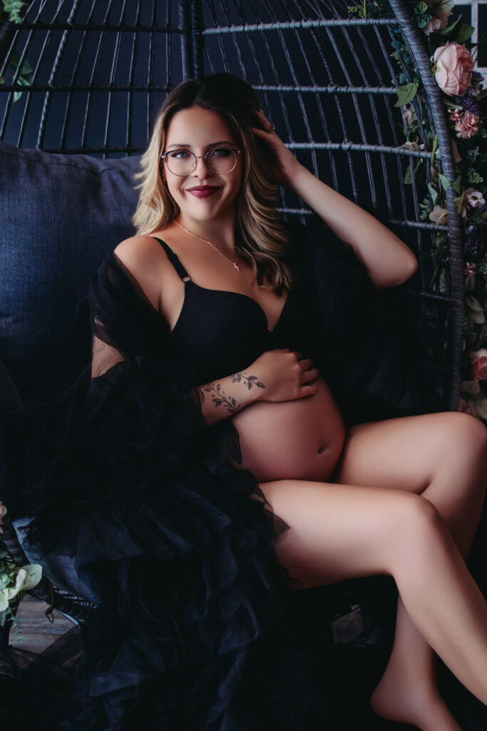 Maternity Boudoir Photography – a glowing pregnant woman smiling while sitting in a cozy chair.