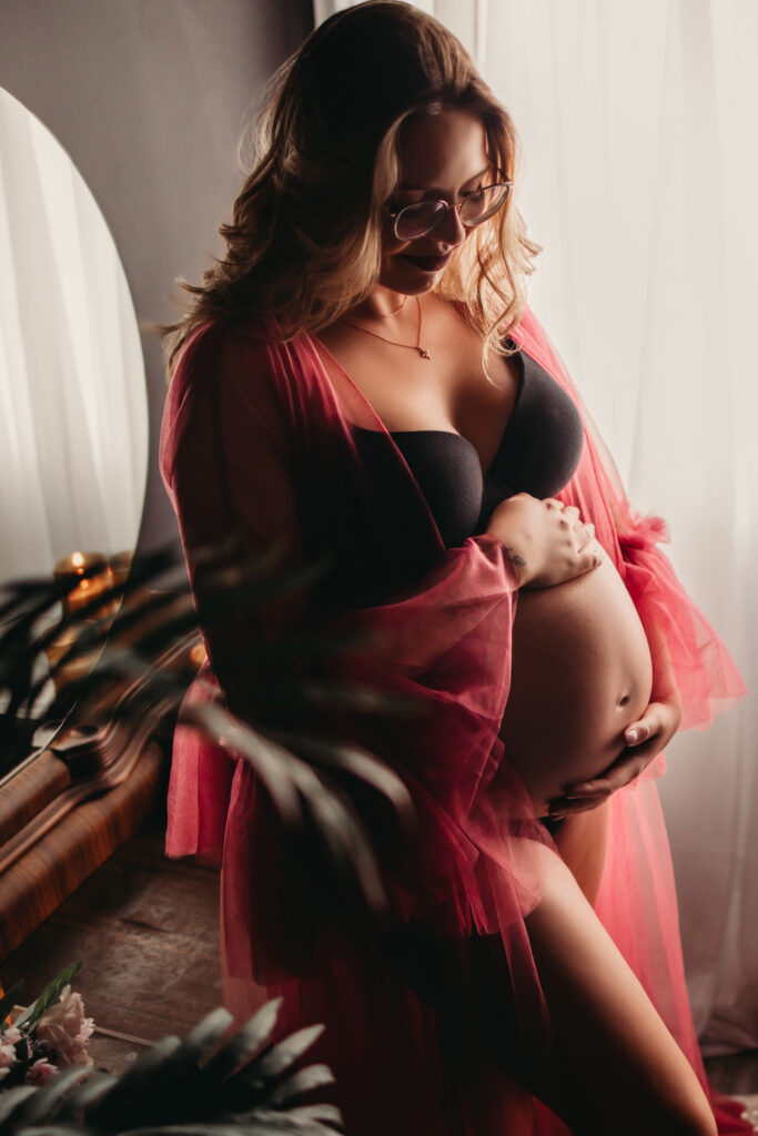 Pregnant woman in a sheer pink robe, cradling her baby bump.